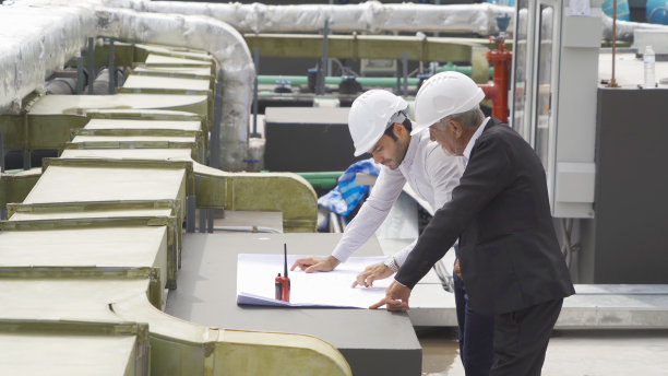 工程师或工人团队，在工业工厂工作的人。屋顶建筑上的冷却塔。系统工作的机器。冷凝器供水管路。通风式压缩机图片下载