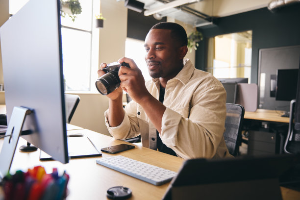 年轻的黑人专业摄影师坐在桌子上工作在电脑上拿着相机编辑图片图片下载