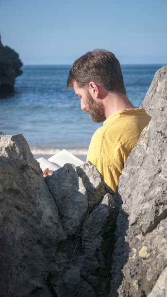 一个男人在岩石海滩上看书图片下载