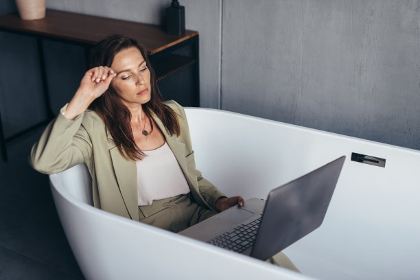 一个女人穿着西装坐在浴缸里，看着她的笔记本电脑屏幕图片下载