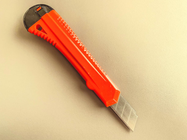 办公室桌子上的文具。有红色塑料柄的文具刀。剪纸，工作工具。白色哑光背景上的刀图片下载