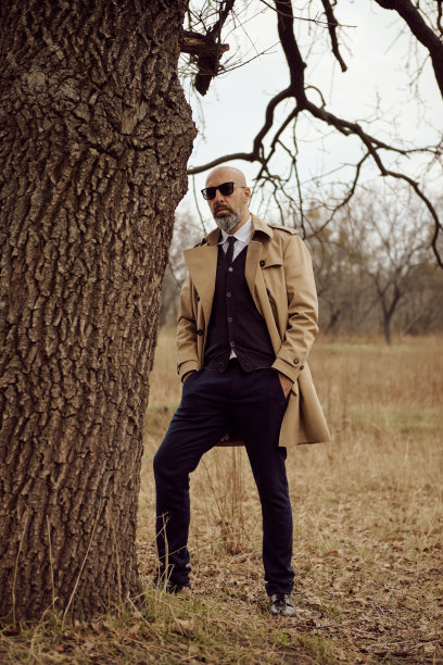 秋天，在公园的一棵树旁，一个穿着风衣的男人的肖像图片下载