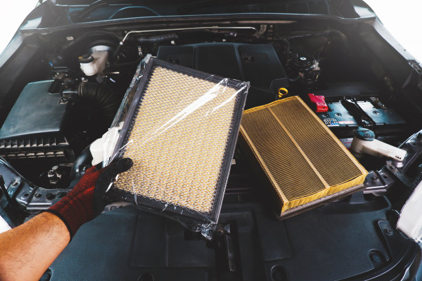 一个汽车修理工拿着一个全新的空气过滤器，它被塑料和肮脏的旧空气过滤器包裹着。图片下载