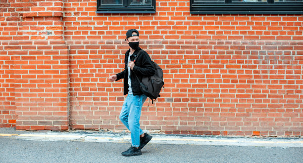 年轻时尚男士青年休闲戴着黑色防护面具走过城市夕阳。时髦的少年在城市里散步冠状病毒大流行。图片下载