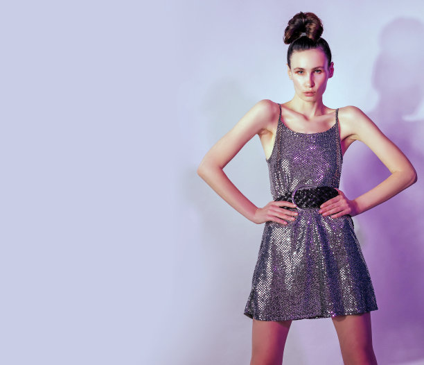 时尚年轻女子在五颜六色的明亮的霓虹灯下摆姿势或跳舞，在灿烂的裙子打个结，光泽的脸在紫色的颜色的光在粉红色的背景图片下载