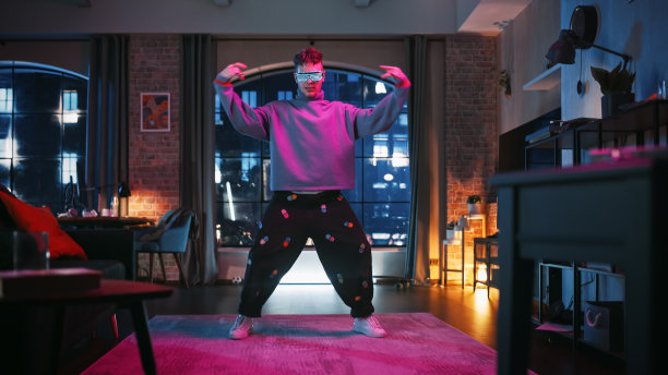 一个英俊的年轻人在时尚的未来霓虹灯发光眼镜跳舞的肖像，有一个在家里的阁楼公寓派对。为社交媒体录制有趣的病毒式视频。图片下载