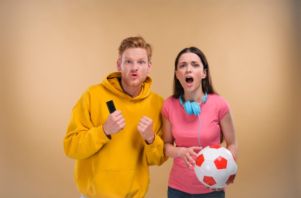 年轻夫妇男人和女人高兴的足球欢呼在米色背景的足球比赛图片下载
