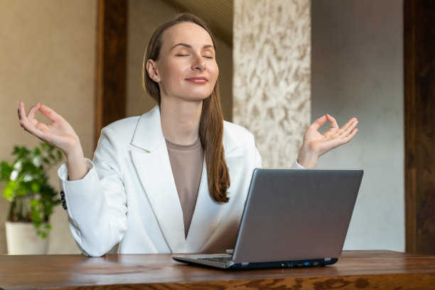 一位穿着白色夹克的年轻女商人坐在办公室的桌子上，以莲花姿势冥想图片下载