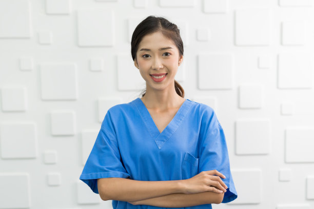 快乐的亚洲护士穿着蓝色制服，双臂交叉站在医院。图片下载