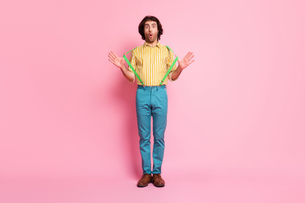 全尺寸的照片，年轻英俊的震惊惊讶的男子拉背带裤孤立在粉红色的背景图片下载