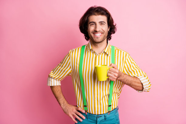 年轻快乐微笑开朗积极的男人的照片拿着马克杯喝咖啡茶早安孤立在粉红色的背景图片下载