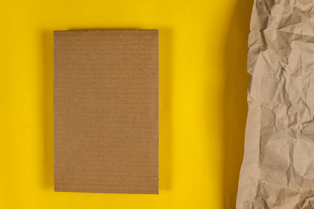 黄色背景的长方形棕色硬纸板。照片右边的包装纸被弄皱了。复制文本和设计元素的空间。前视图。图片下载