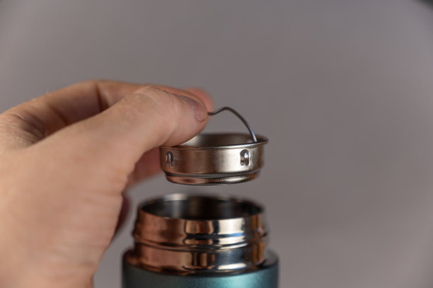 一个男人的手把茶壶插入保温杯的颈部。银色的啤酒壶和闪亮的螺纹颈现代保温杯。绿松石色圆柱形保温瓶。冷热饮料的容器图片下载