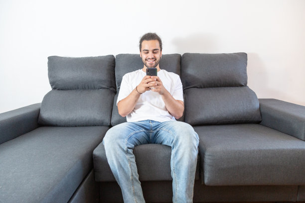 年轻人坐在沙发上玩手机。图片下载