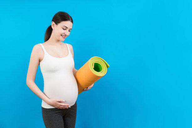 抱着瑜伽垫的怀孕女孩站在彩色背景上。工作室拍摄，设计的自由空间图片下载
