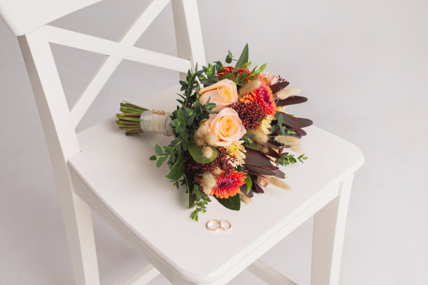 结婚戒指放在白色的椅子上，背景是花束。婚礼仪式。摄影工作室。本空间图片下载