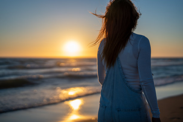 一个女人在海滩上散步时看日落图片下载