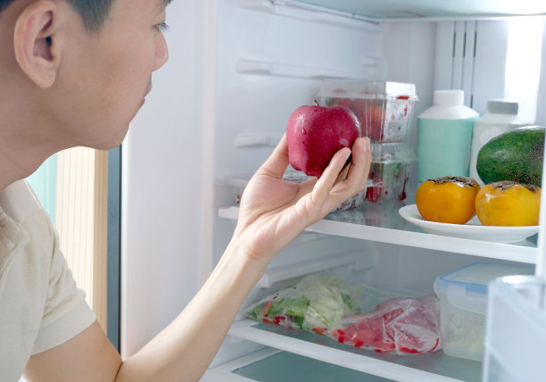 男士挑选健康食材，捧着一个红苹果做健康食品。健康食品包括冰箱里的水果、蔬菜、苹果、草莓、番茄和葡萄。图片下载