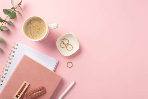 经营理念。工作空间的顶部视图照片粉红色的规划师钢笔时尚的发夹金戒指杯咖啡和桉树在孤立的粉红色背景与copyspace图片下载