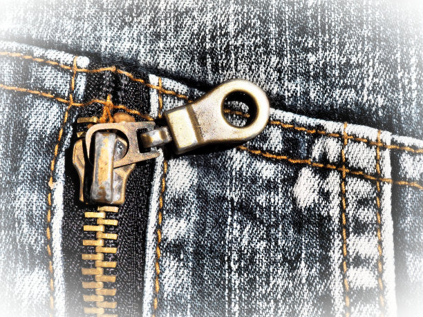 特写牛仔布与接缝和锁。破旧不堪的牛仔裤金属青铜黄色带转轮锁紧。垂直接缝。图片下载