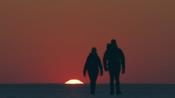 两个游客在美丽的夕阳下穿过雪地图片下载