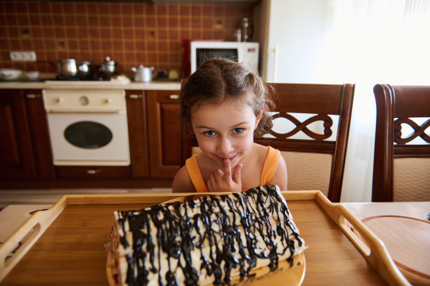 可爱的欧洲小女孩看着镜头后面一个模糊的樱桃巧克力派在乡村舒适的木制厨房内部图片下载