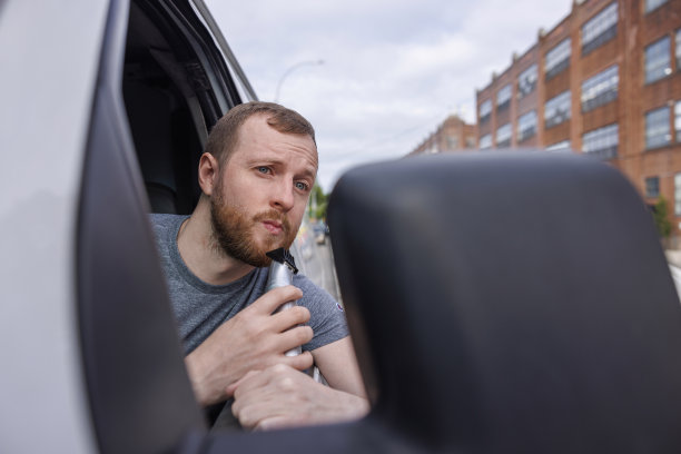 一名司机在停在街上的卡车里用后视镜和便携式修剪器刮胡子。图片下载