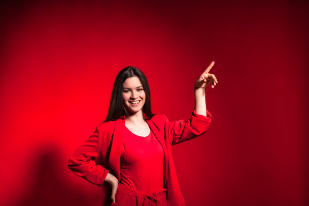 肖像十几岁的女孩在时尚的服装在红色背景看相机，并指出图片下载