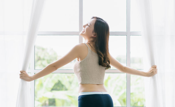 幸福美丽性感的亚洲女人清晨醒来，打开窗户白色的窗帘，望向窗外，感觉清新与微笑的脸，在家里度过空闲的时间舒适。生活方式的概念。图片下载