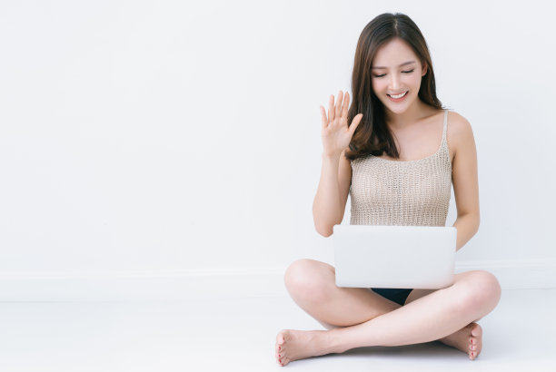 美丽性感的亚洲女性微笑着友好地使用笔记本电脑，在线视频通话广播，会见博主，坐在家里的地板上，为朋友或粉丝向她的博客打招呼。图片下载