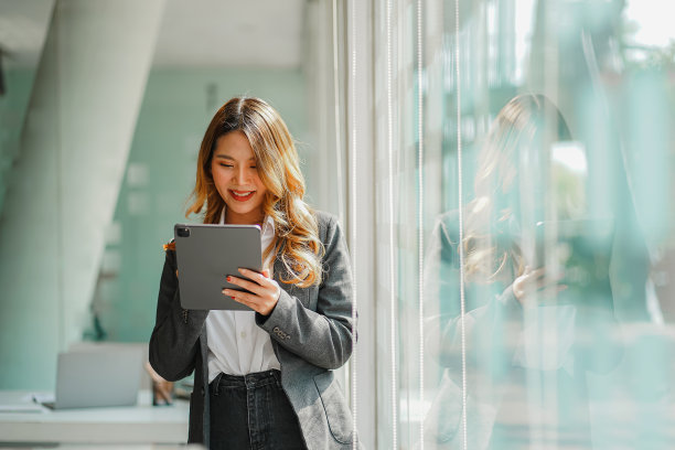 亚洲女商人站在办公室玻璃墙旁边的平板电脑图片下载