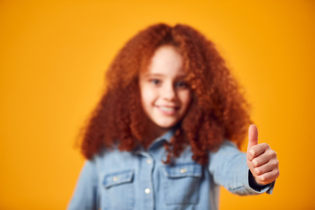 工作室肖像微笑的年轻女孩做竖起大拇指的手势拍摄的黄色背景图片下载