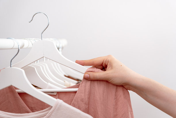 在时装店的衣架上，女人用手挑选要买的衣服，特写。图片下载