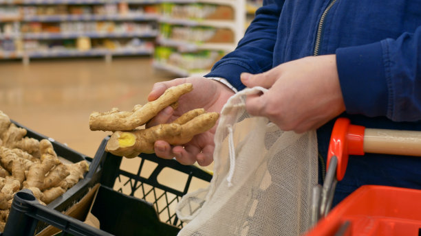 一个男人在商店里买了治疗感冒和传染病的姜。在当地市场购买新鲜的水果和蔬菜。商店货架上有精选的酸橙和苦艾根。图片下载