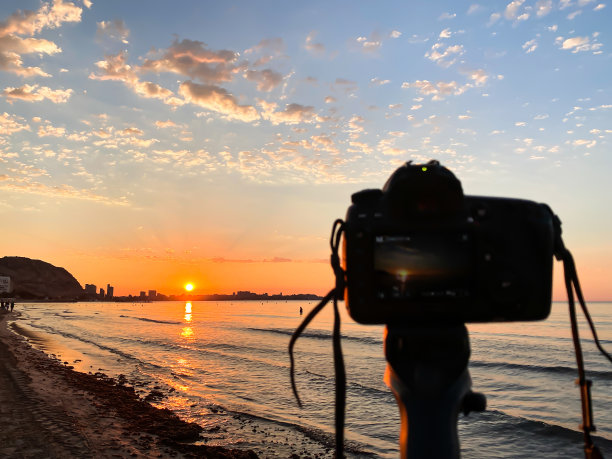 三脚架上的相机在海滩上拍摄日出的照片，因为这是摄影的日子。图片下载