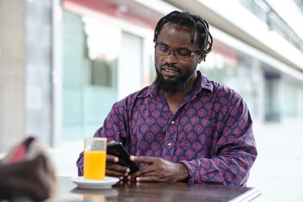 一个漂亮的黑人男子在户外的桌子上用他的智能手机拍的中号照片图片下载