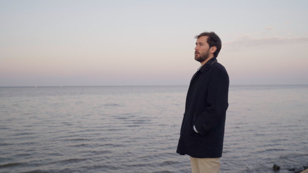 一个穿大衣的年轻人在河边看日落时的地平线图片下载