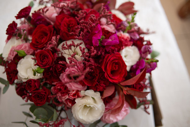 花束自然清新，花朵颜色鲜艳，有马沙拉，白色，红色，粉色和绿色的芽叶。花束放在木桌上。特写照片与相机变焦。图片下载