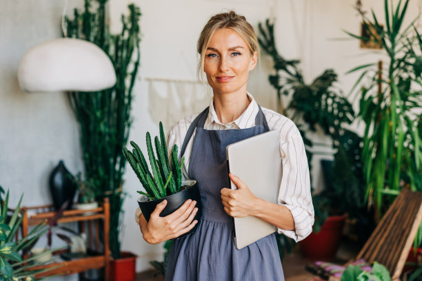 一位女企业家站在车间里，手里拿着笔记本电脑和盆栽。图片下载