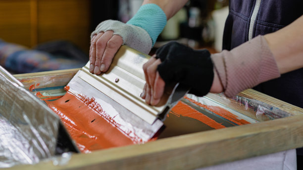 有橡胶清洁器的男性手。在车间的t恤上创作印花。绢网印花印刷生产。丝网纺织品印刷图片下载