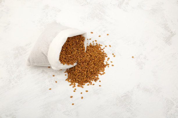 胡芦巴的种子从白色的袋子里洒到了桌子上。香巴拉或海尔巴种子是传统的印度调味料和阿育吠陀食物的成分图片下载