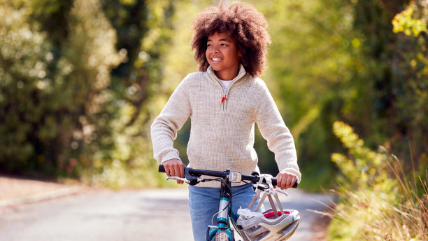 带安全帽的微笑男孩沿着乡村道路推自行车图片下载