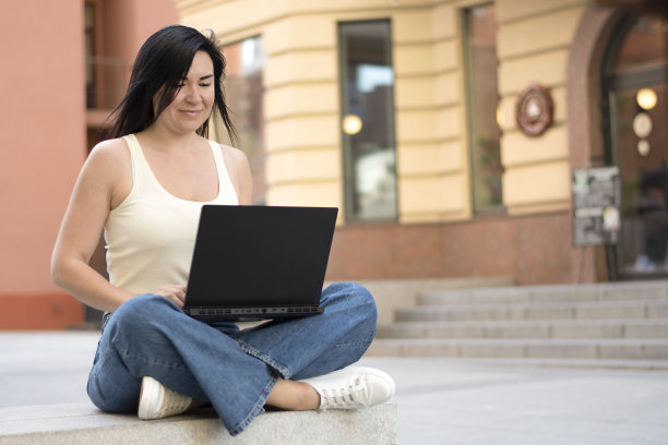 人。一个年轻漂亮的白人女孩坐在公园的长椅上，手里拿着笔记本电脑。的概念。图片下载