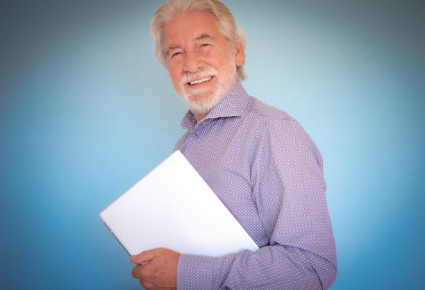 微笑的大胡子老人手持笔记本电脑看着相机。年老美丽的商人或老师去工作图片下载