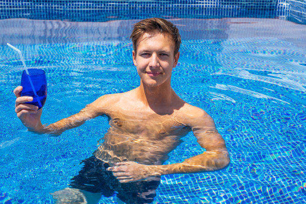 水池里一个人手里拿着一根吸管的蓝色玻璃杯水。暑假与健康理念图片下载