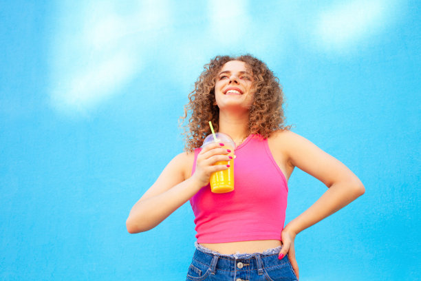 美女捧着美味的橙汁，清凉爽口的夏日饮品。蓝色背景,孤立。在户外，在城市里走走。本空间图片下载