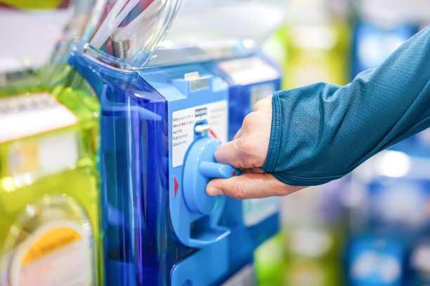 一个穿着绿松石毛衣的人的手正在扭动一个蓝色的gashapon机器，释放出一个数字。在日本，它被认为是最受欢迎的风险之一。图片下载