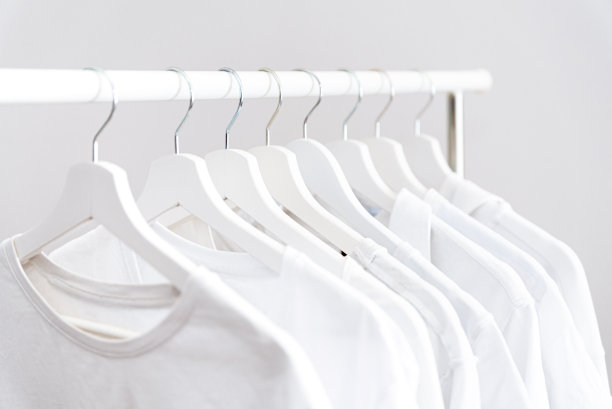 白衣服一行行挂在白色衣架上。极简衣橱，便携式衣架上有许多衣架图片下载