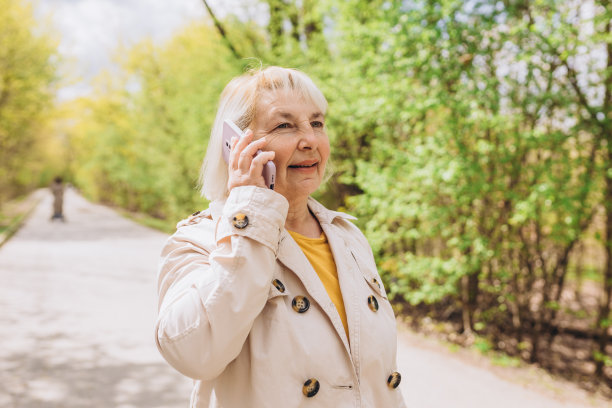 美丽成熟的女人在时尚的穿着花时间在公园和使用智能手机。开心学长煲手机粥，春日艳阳天。城市生活理念，科技旗帜图片下载
