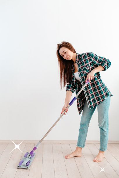 清洁的概念。年轻的白人妇女微笑着洗地板。背景中有一面白色的墙。空气中洁净的白色星星。垂直图片下载